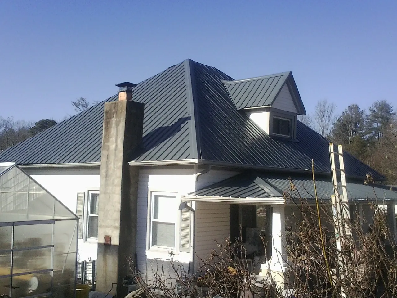 Dark blue standing seam metal roof on a white farmhouse with dormer — Slate & Tile Roof Repair by Roofing Brothers in Chapel Hill