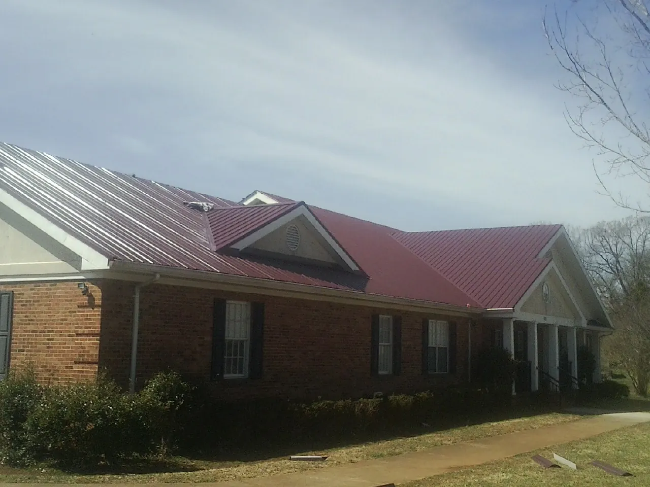 Red metal roof with gabled entries on a long brick building, from a Hail Damage Roof Repair job in Chapel Hill