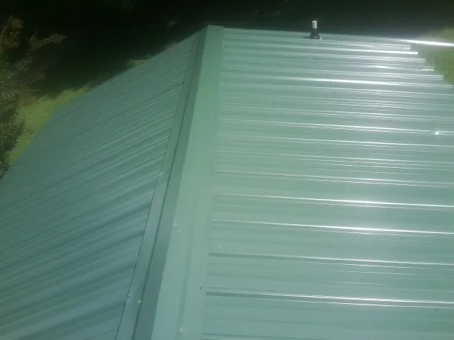 New green metal panels meeting at the ridge of a roof — Flat Roof Repair work by our crew in Chapel Hill
