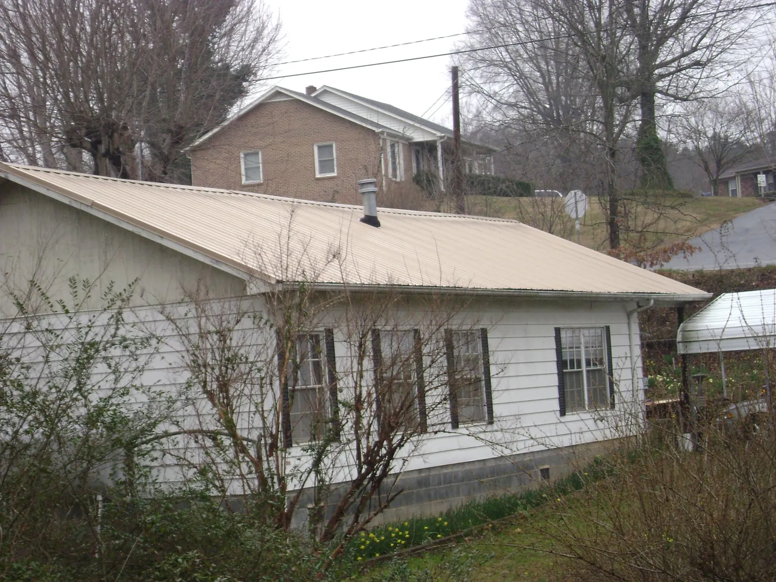 Tan metal roof on a white sided house set into a hillside — Commercial Roofing by Roofing Brothers in Chapel Hill
