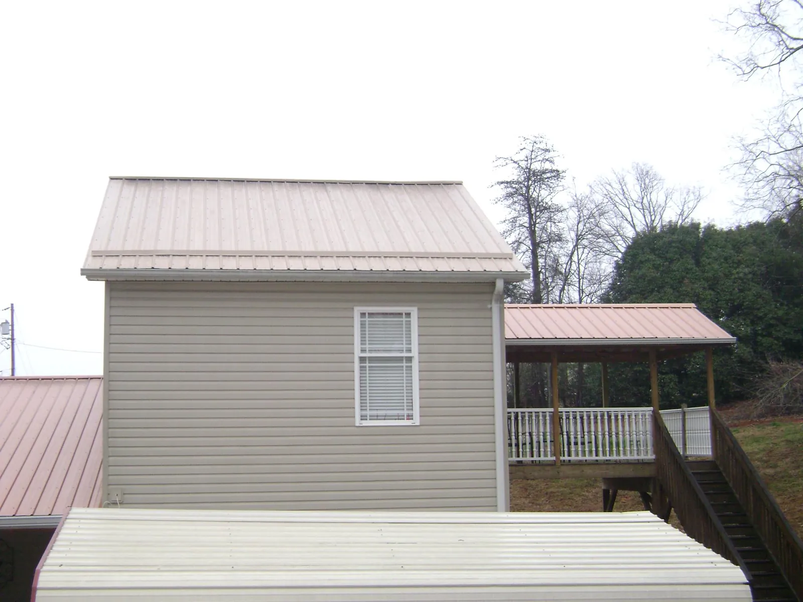 Tan metal roofs on a two story addition and attached porch, from a Roof Replacement job in Chapel Hill