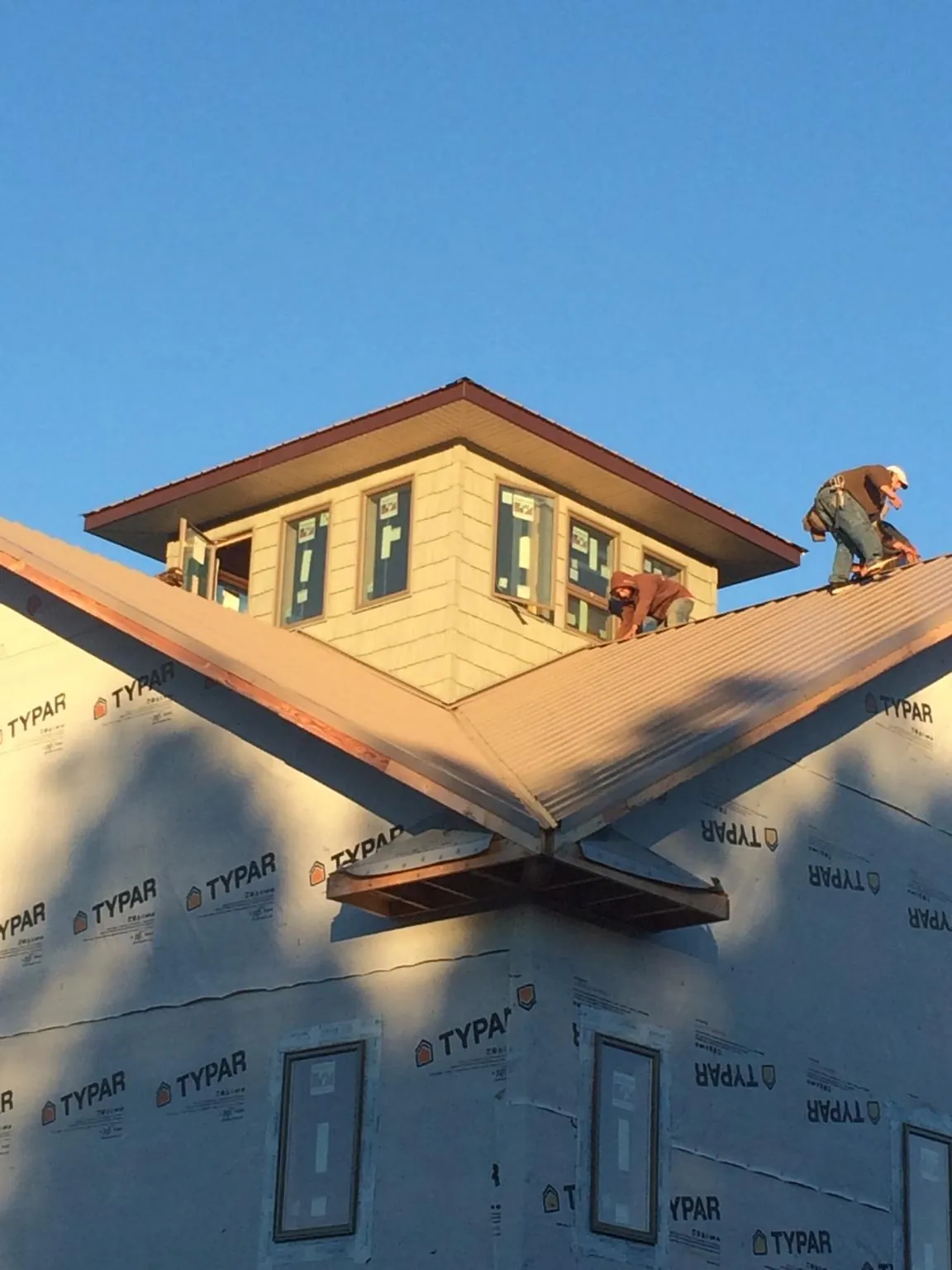 Roofers working around a rooftop cupola on a new metal roof at sunset — Roof Waterproofing in Chapel Hill by Roofing Brothers